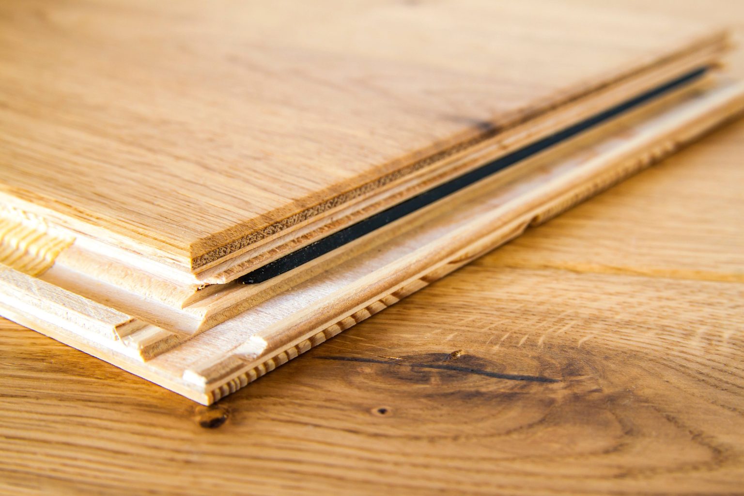 A close up view of a wooden board with a measuring tape laying on a hardwood floor