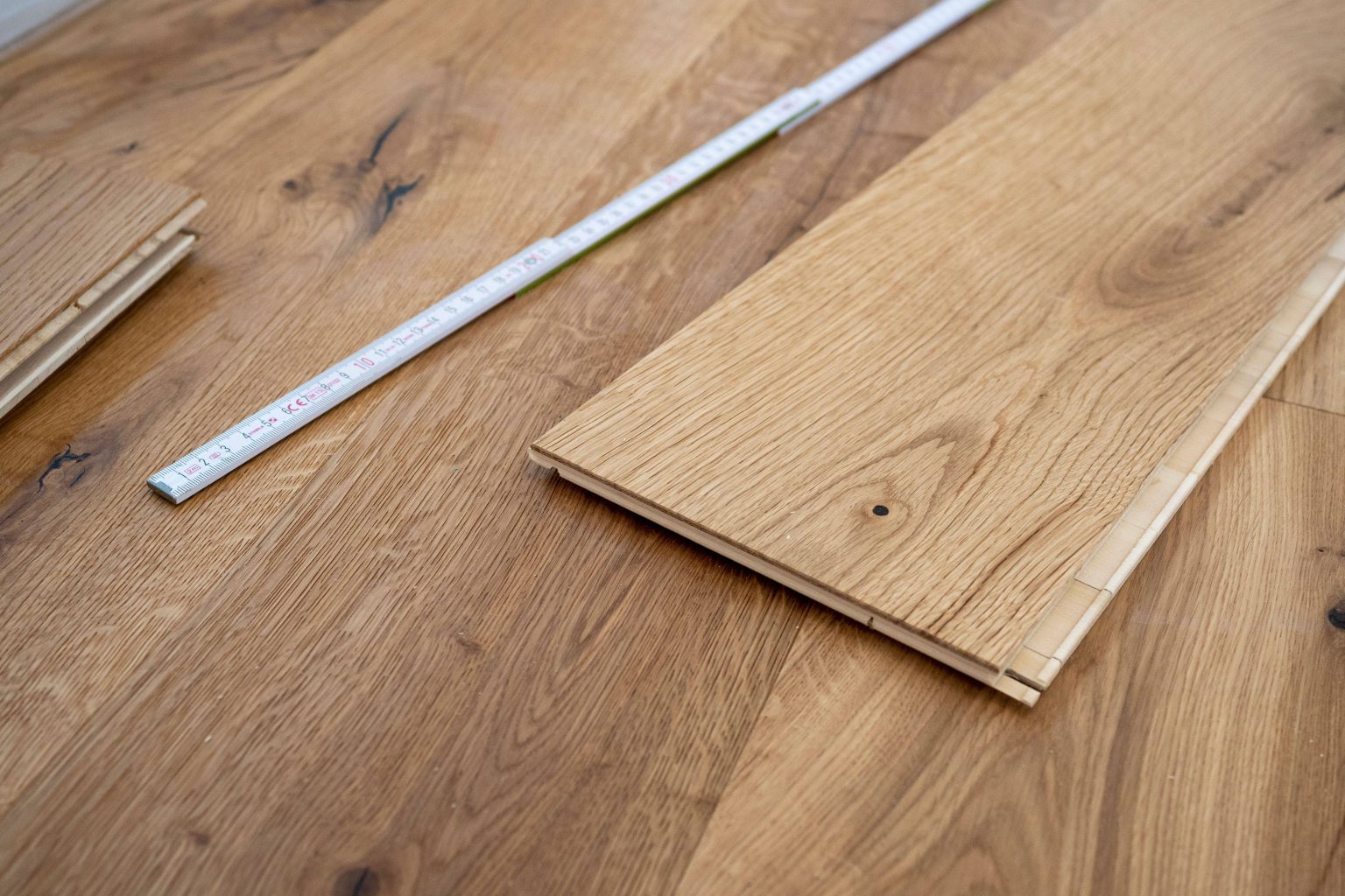 A close up view of a wooden board with a measuring tape laying on a hardwood floor